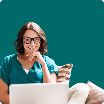Mulher branca, sorridente com óculos e cabelo castanho, vestindo uma blusa verde-água, sentada em um sofá com um laptop no colo e a mão no queixo, em frente a um fundo verde-água sólido.